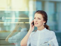 Pretty young business woman with newspaper using mobile phone