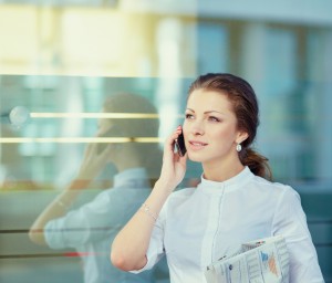 Pretty young business woman with newspaper using mobile phone